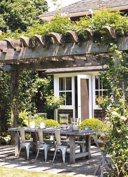 an outdoor dining table and chairs under a pergolated arbor with potted plants