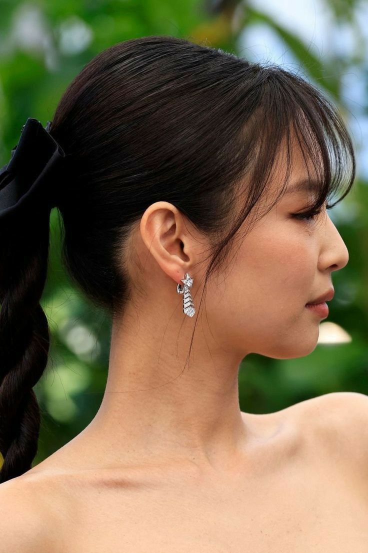 a woman with long black hair wearing large silver ear clips and a bow in her hair