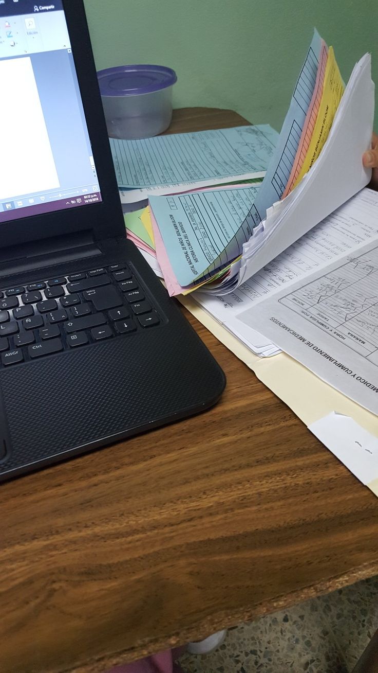 an open laptop computer sitting on top of a wooden desk next to papers and pens