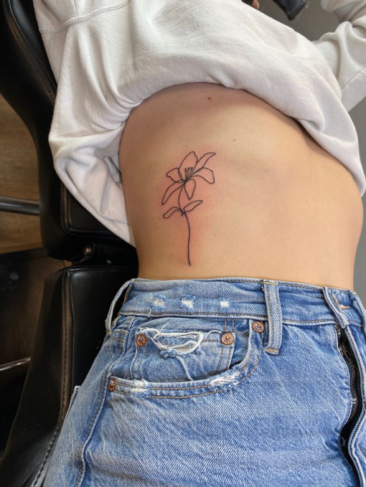 a woman's stomach with a small flower tattoo on her lower side ribcage