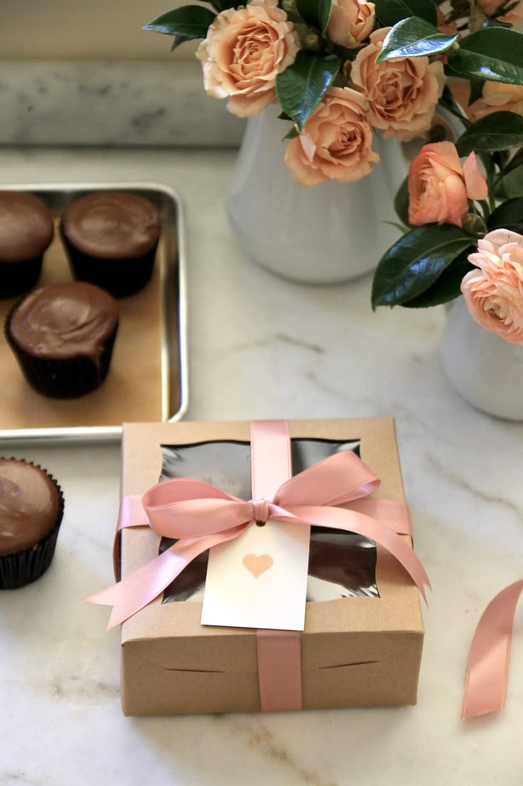 some cupcakes are sitting on a table next to flowers and a vase with roses