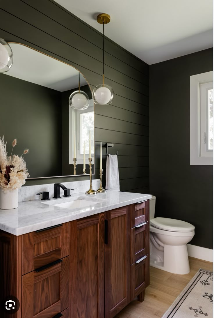 a white toilet sitting next to a bathroom sink under a mirror on top of a wooden cabinet