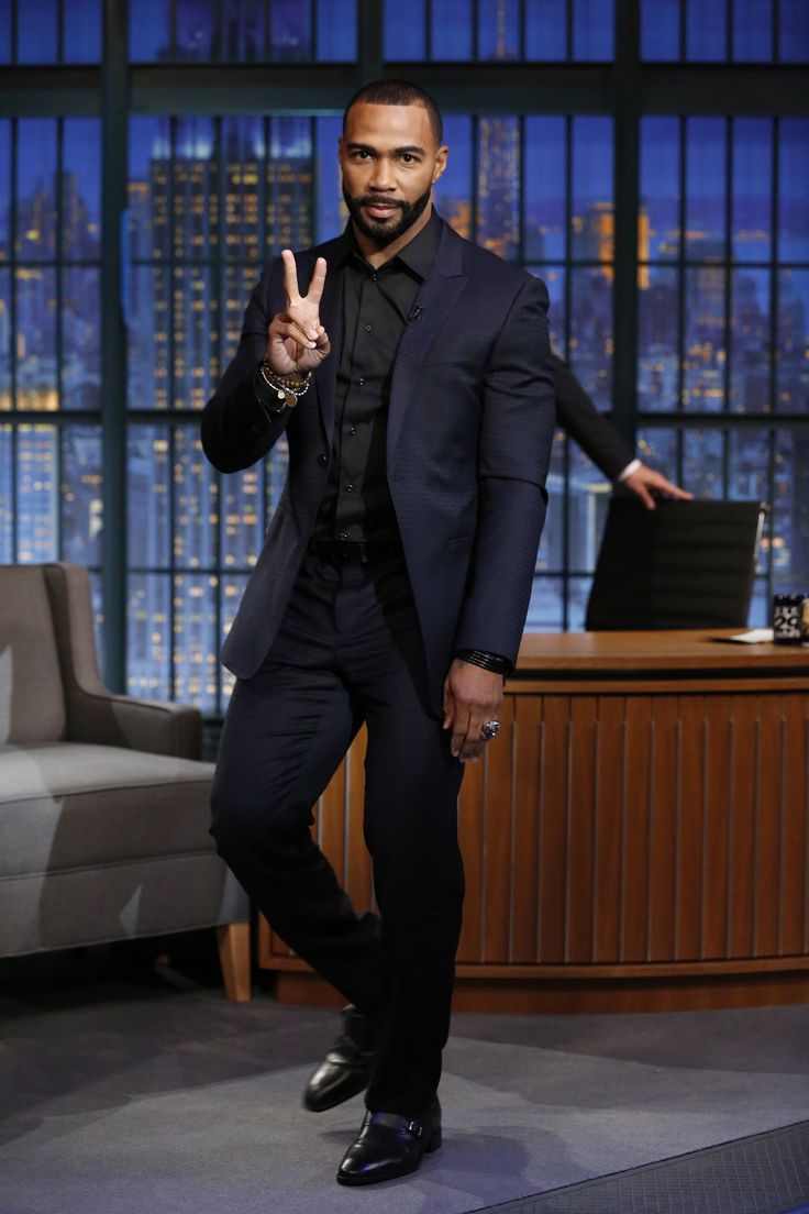 a man in a black suit and tie making the peace sign on stage with his hand