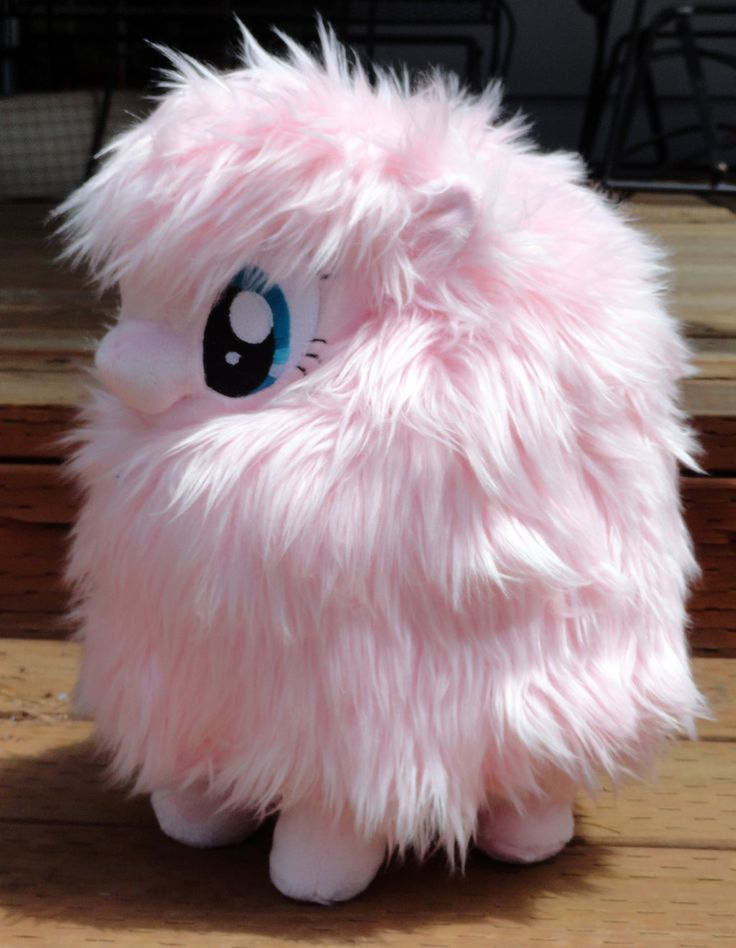 a pink stuffed animal with blue eyes sitting on top of a wooden table