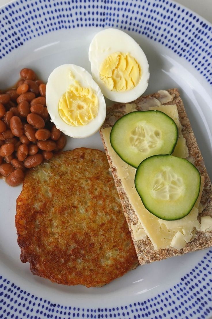 a plate with some food on it including eggs, bread and beans next to sliced cucumbers