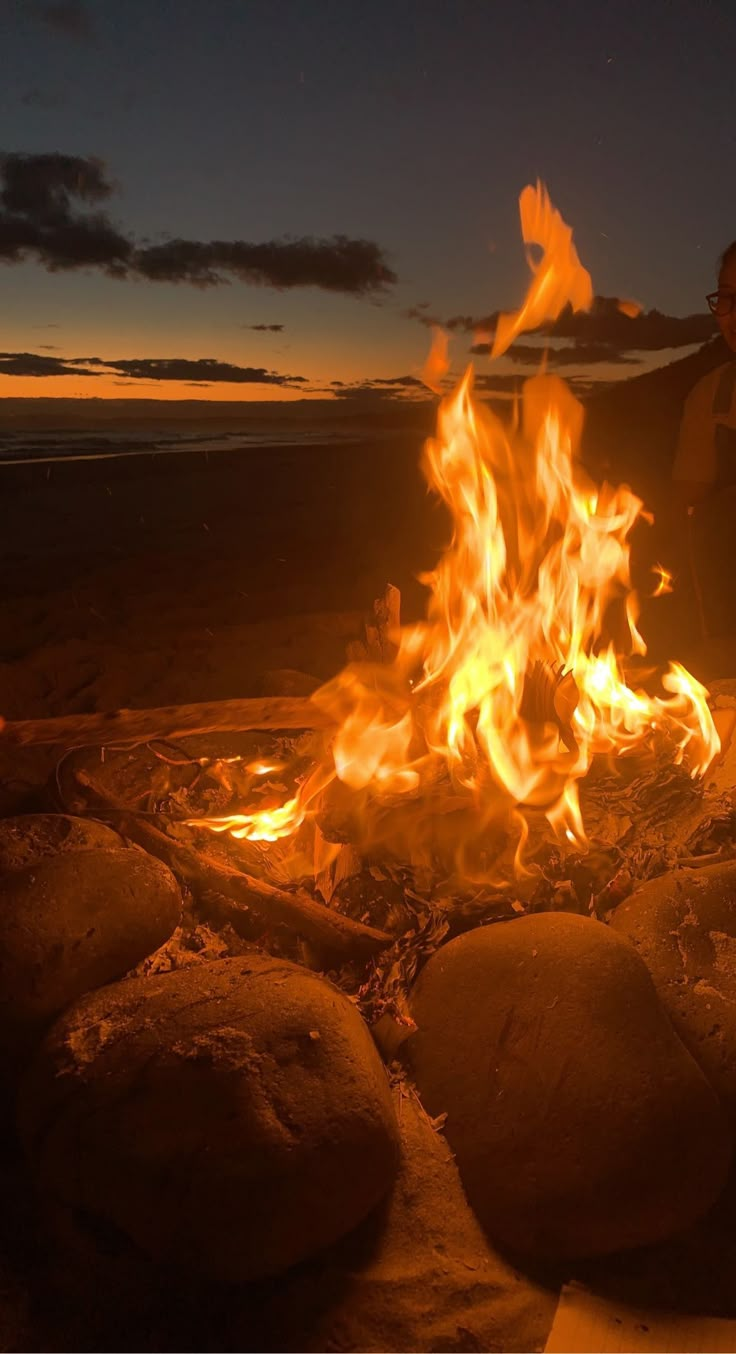 a person standing in front of a fire with rocks on the ground next to it