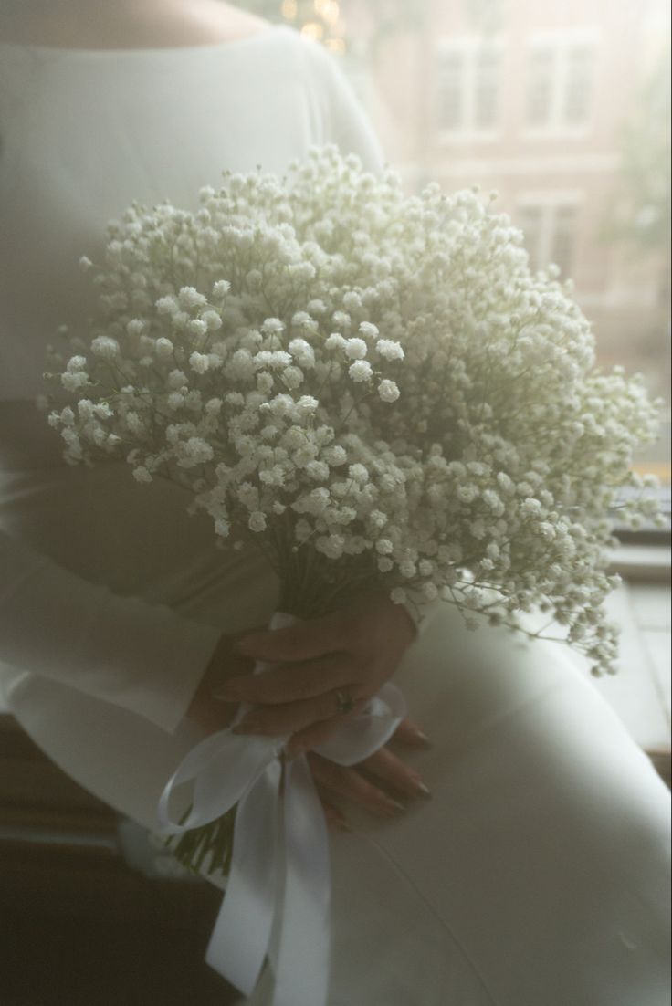 a bride holding a bouquet of baby's breath in front of a window sill