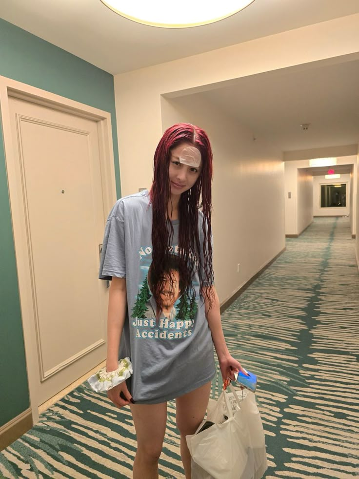 a woman with red hair is holding a bag and looking at the camera while standing in an empty hallway