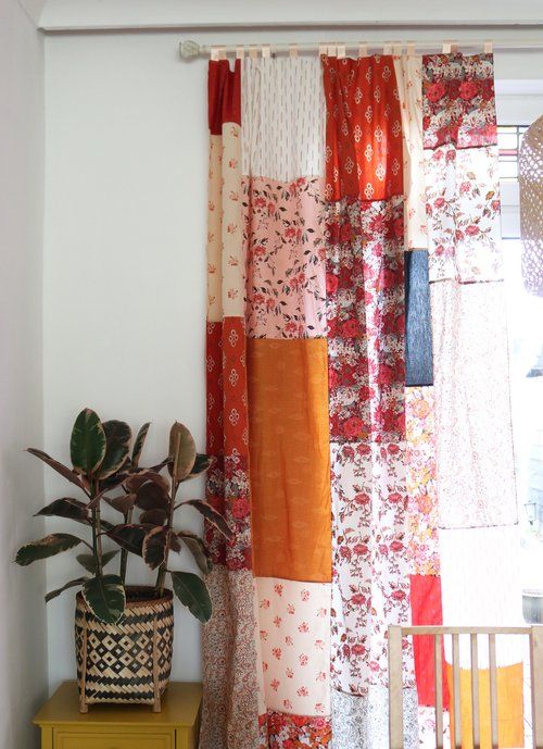 a potted plant sitting next to a window covered in multicolored fabric curtains