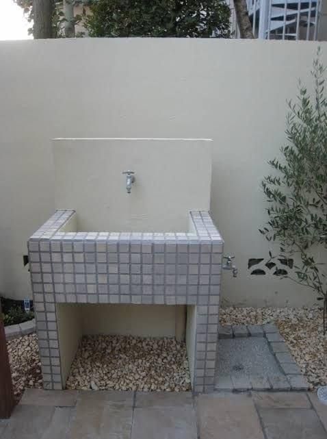 a white sink sitting on top of a tiled counter next to a tree and bushes