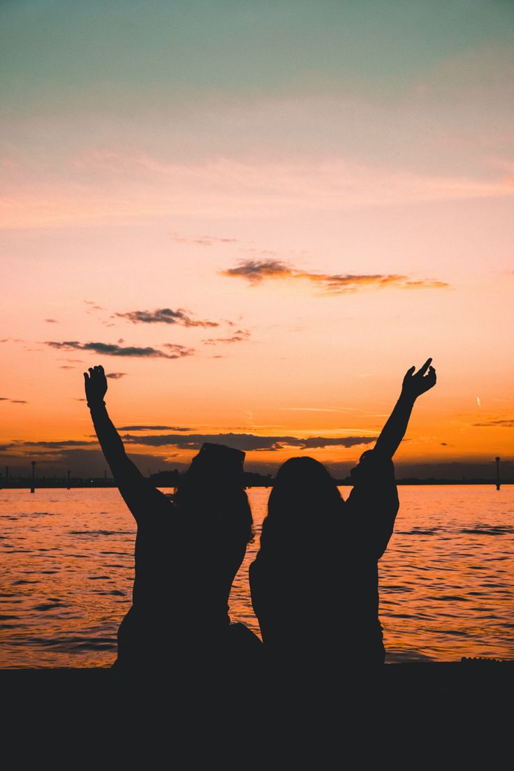 two people sitting on the beach with their arms in the air