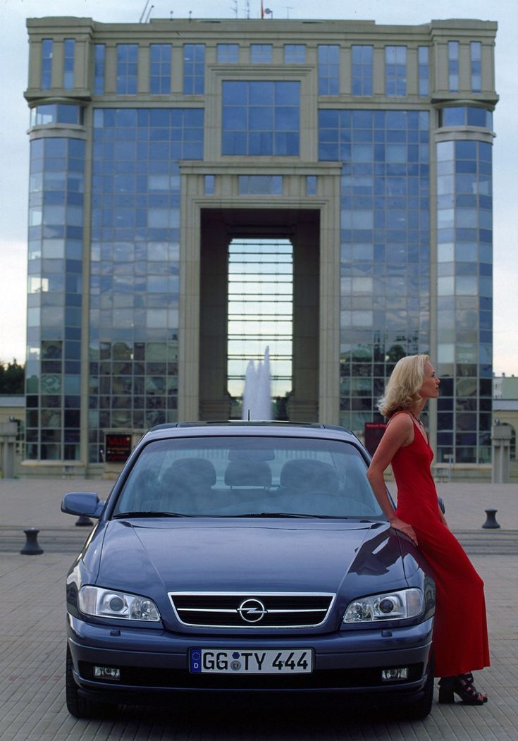 a woman in a red dress standing next to a blue car