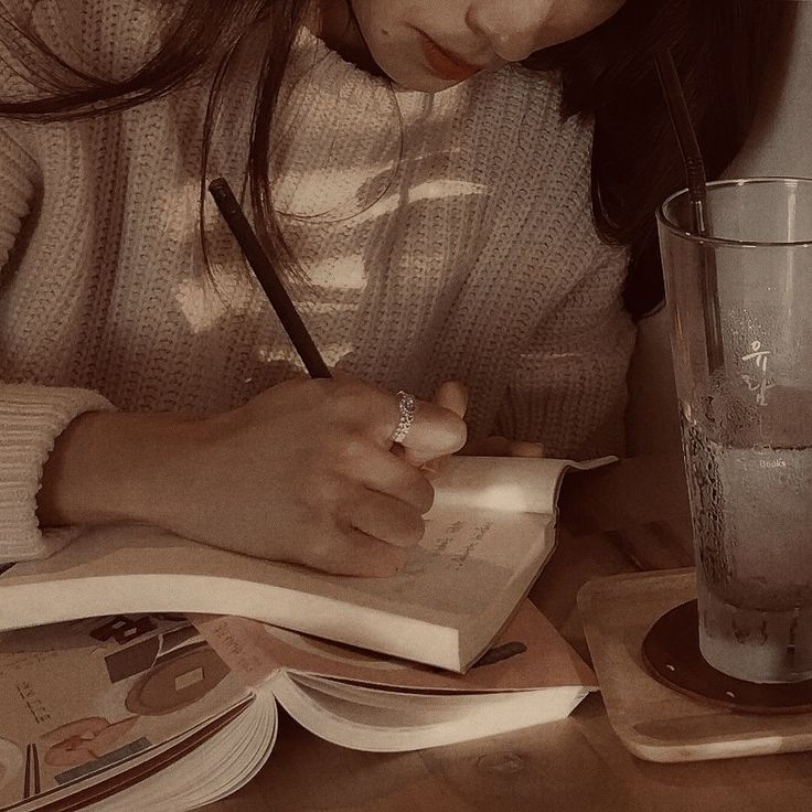 a woman sitting at a table with a book and pen in her hand while writing