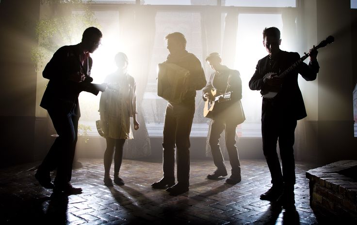 a group of people standing in front of a window holding guitars and looking at each other