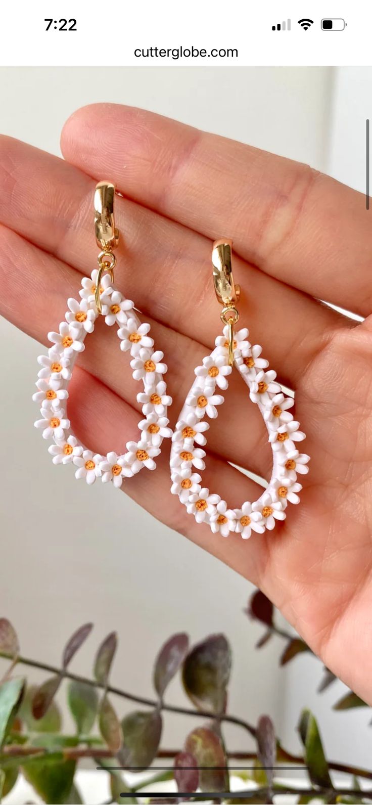 a hand holding a pair of white beaded earrings with gold hoops and pearls