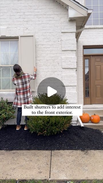 a person standing in front of a house with pumpkins on the ground and bushes