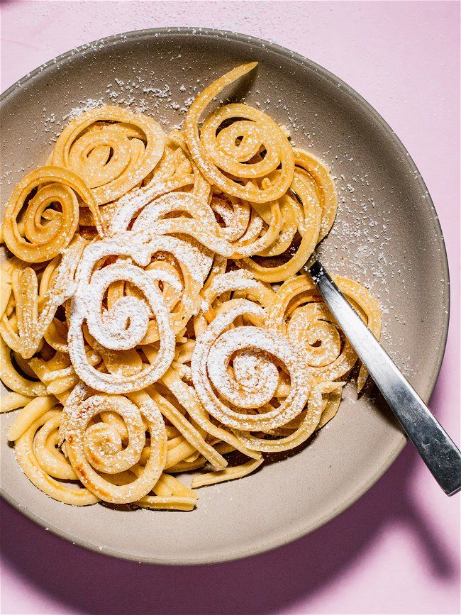 a bowl filled with pasta and powdered sugar on top of a pink tablecloth