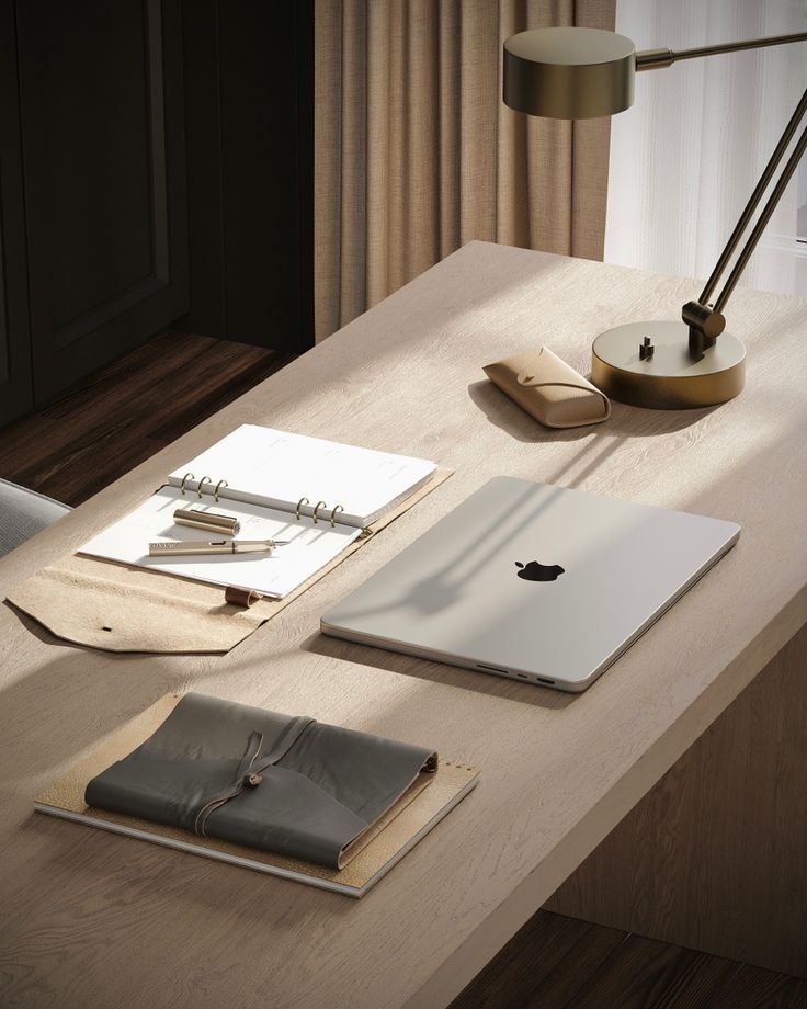 an apple laptop computer sitting on top of a wooden desk next to a lamp and notebook