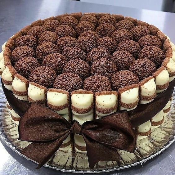 a chocolate cake with white frosting and brown bows on it's edges, sitting on a plate