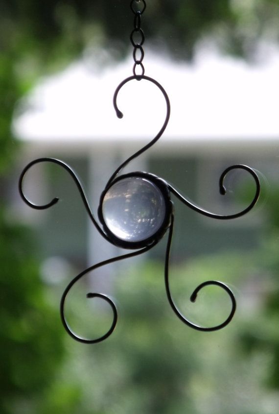 a metal wind chime hanging from a window with green trees in the back ground