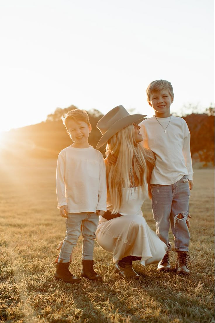 two boys and a girl standing next to each other in a field with the sun behind them