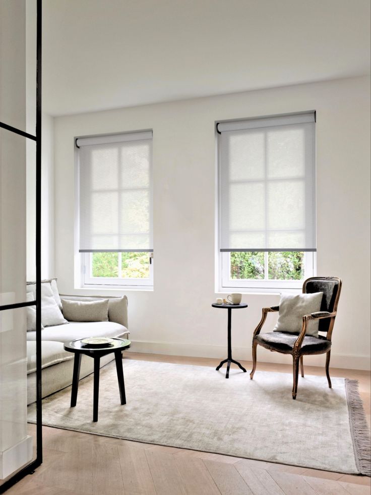 a white living room with two windows and a table in front of the couches