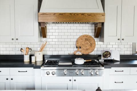 a stove top oven sitting inside of a kitchen next to wooden spoons and utensils