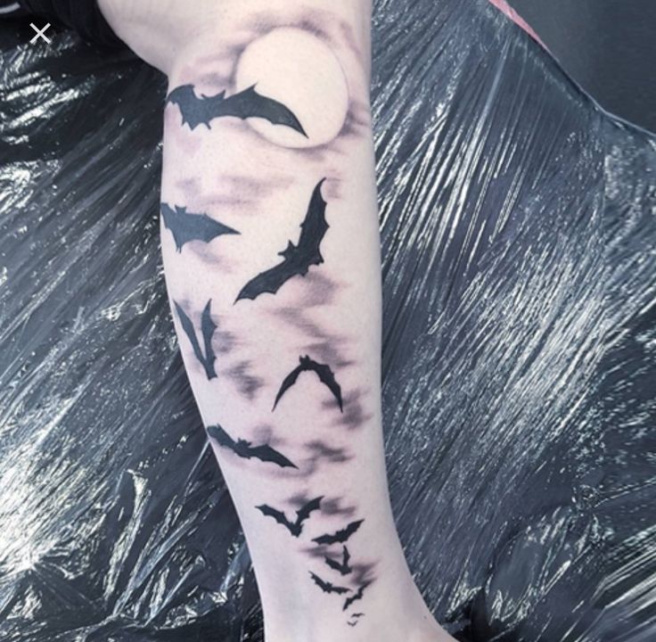 a person with a tattoo on their leg and some bats flying in the night sky