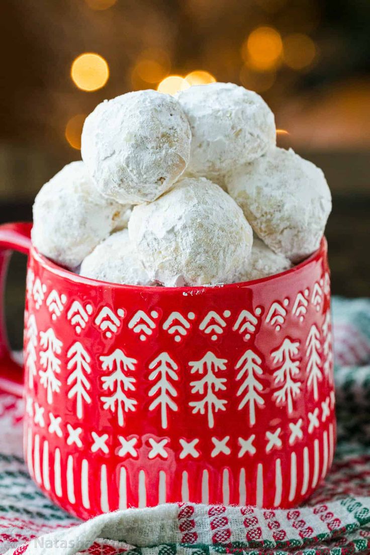 a red bowl filled with snowball cookies on top of a table