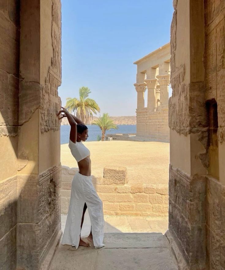 a woman in white dress standing at the entrance to an ancient building with palm trees