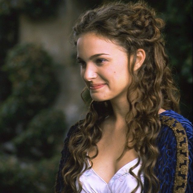 a woman with long curly hair wearing a blue and white dress smiling at the camera