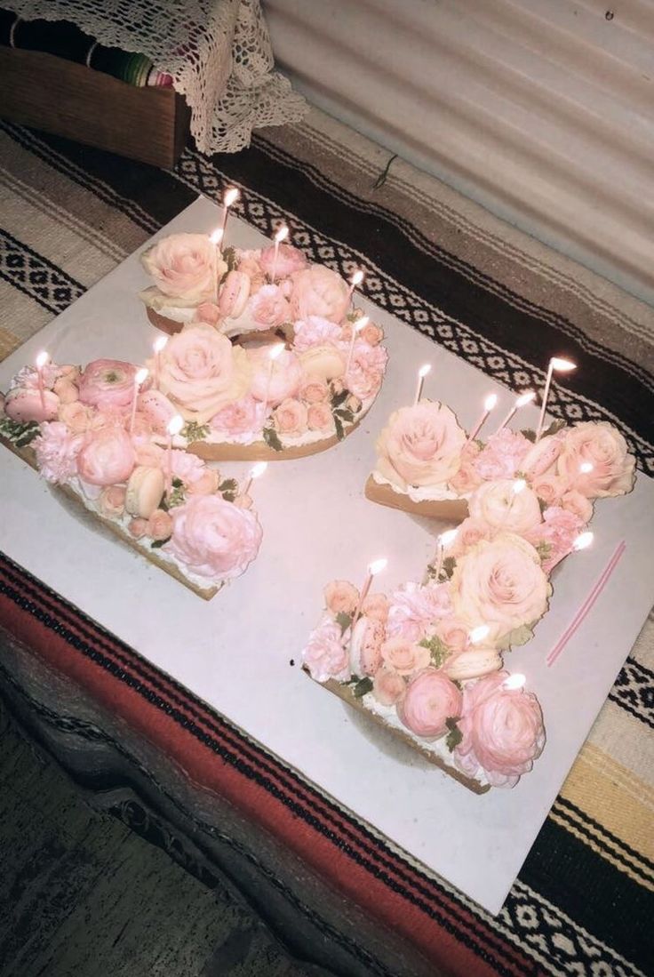 two birthday cakes with candles are on a table in the middle of a room filled with pink flowers