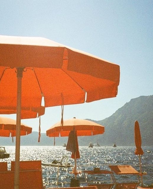 many orange umbrellas and chairs are on the beach by the water with mountains in the background