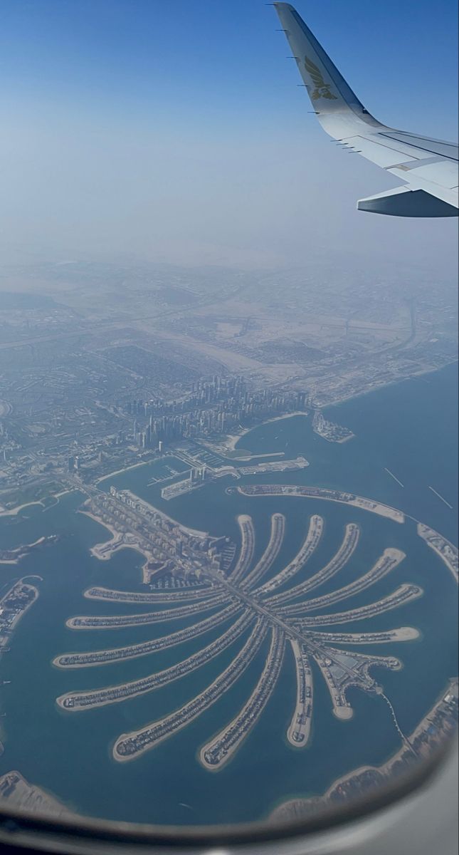 an airplane wing flying over a large island in the ocean with buildings on it's sides