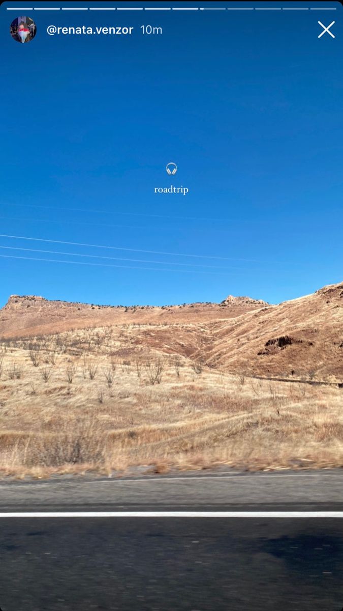 the view from inside a car looking out at mountains and hills in the distance with an airplane flying overhead