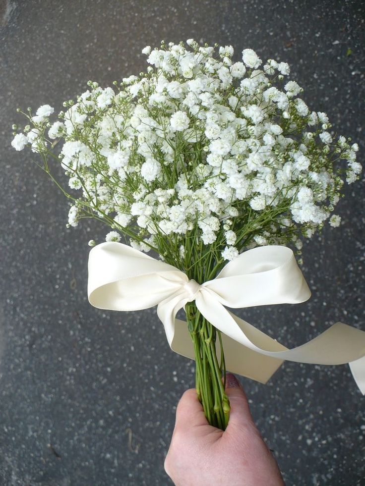 a person holding a bouquet of white flowers with a ribbon around it's end