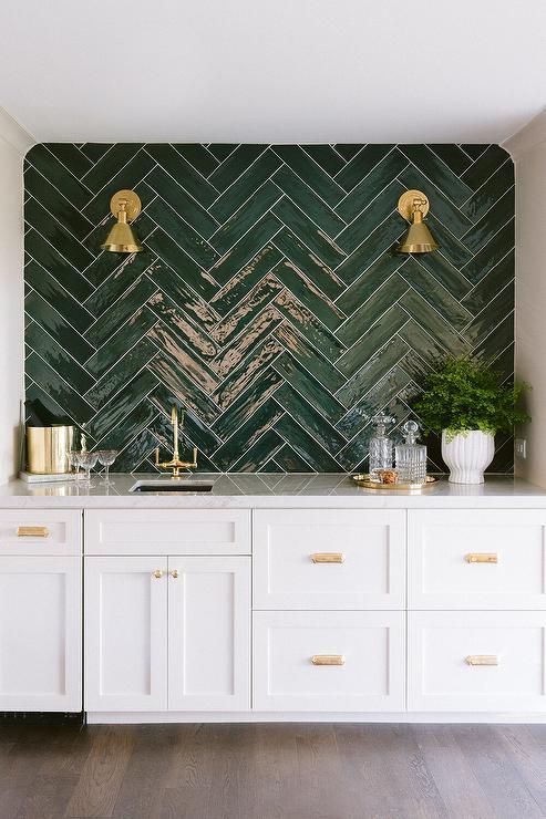 a kitchen with white cabinets and green tile backsplash, gold faucets