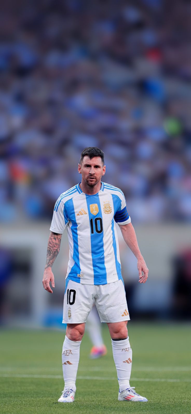 a man standing on top of a soccer field wearing a blue and white uniform with his hands in his pockets