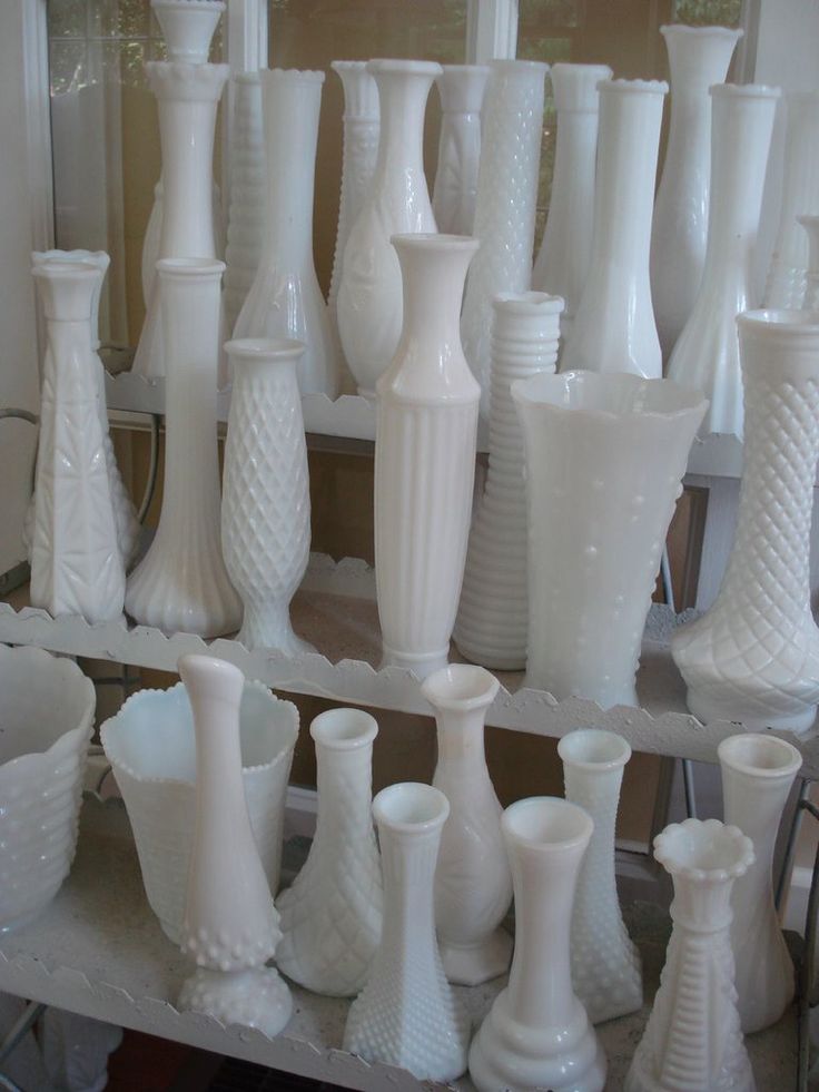 many white vases are lined up on a shelf