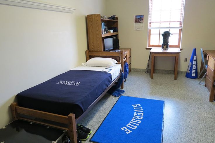 a bedroom with a bed, desk and television in it on the floor next to a blue rug