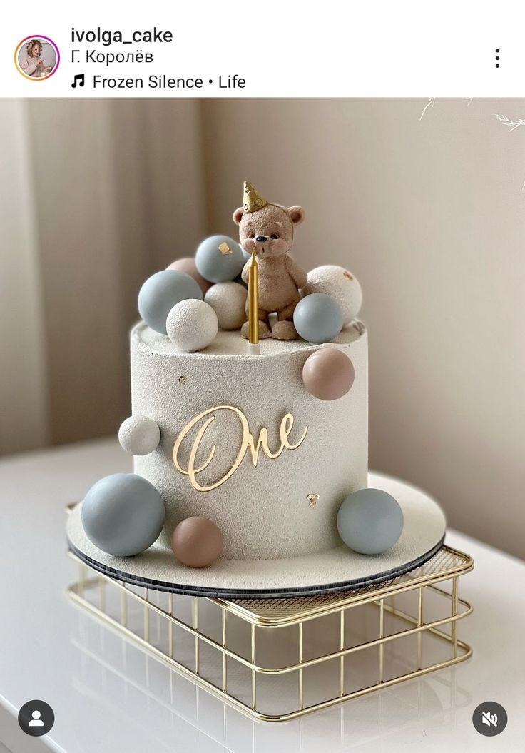 a cake with a teddy bear sitting on top of it and the words one written in gold