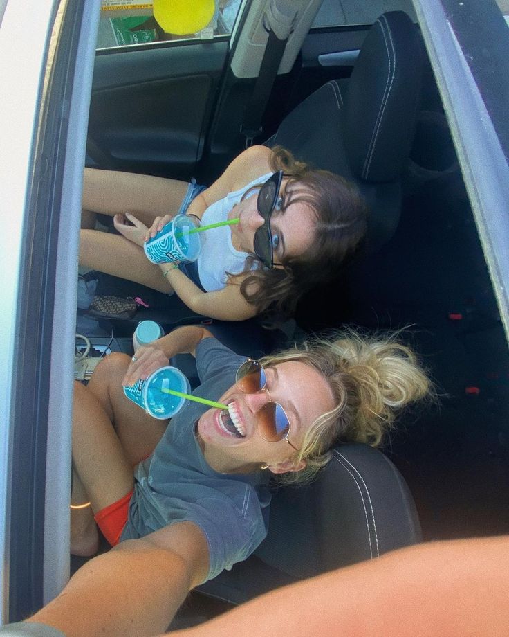 two young women sitting in the back seat of a car drinking water from plastic bottles