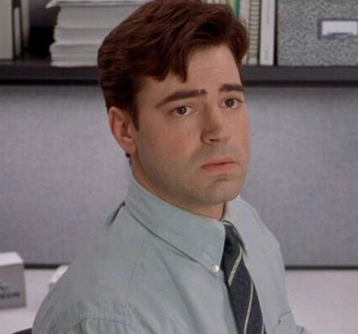 a man sitting at a desk in an office looking to his left with serious expression