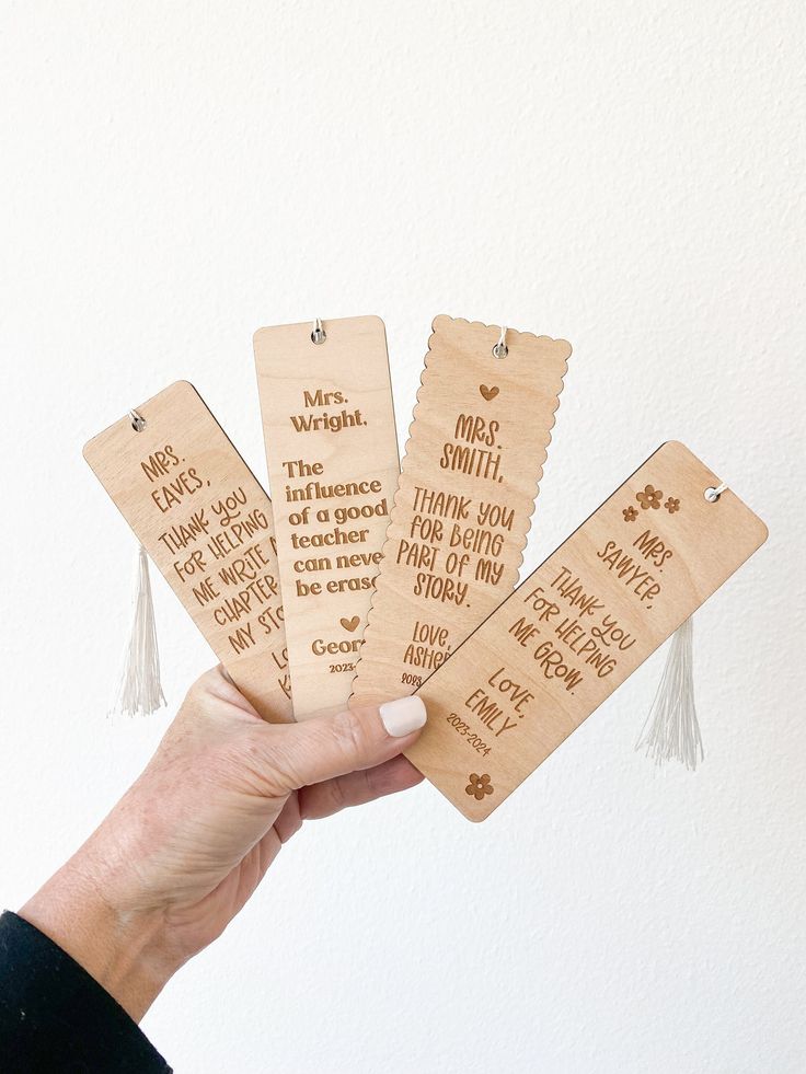 hand holding four wooden bookmarks with writing on them and tassels around the edges