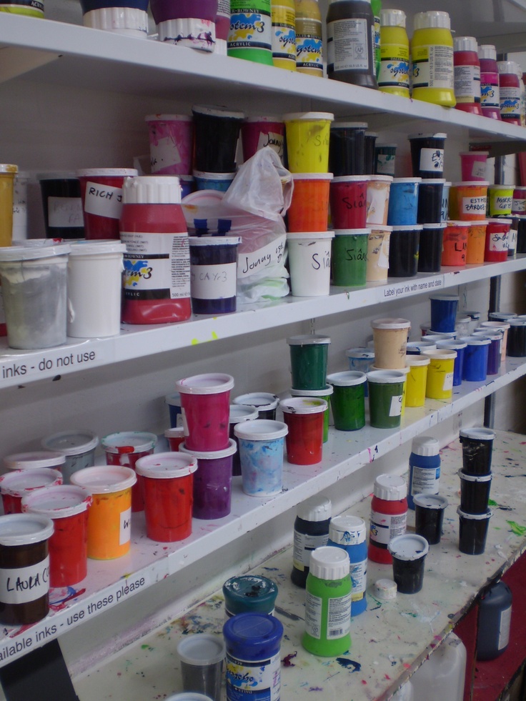 the shelves are filled with many different colors of paint and one is full of cups