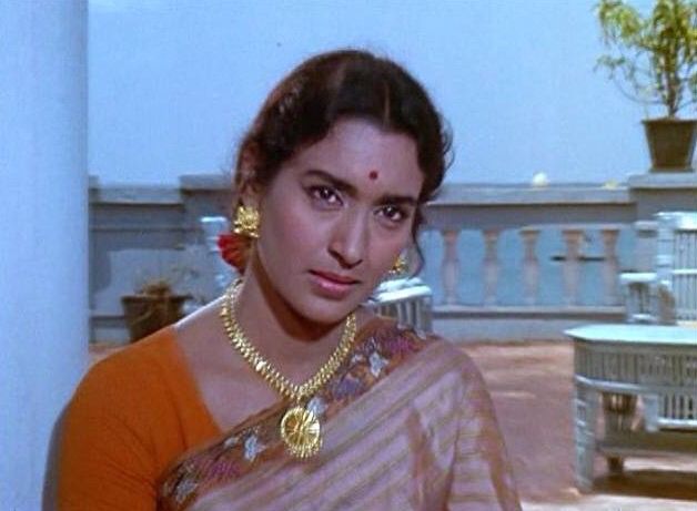 a woman in an orange and white sari with gold jewelry on her neck, looking at the camera