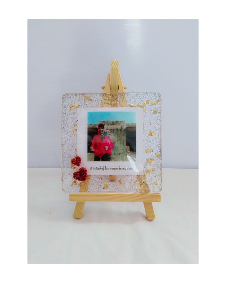 a small wooden easel with a glass frame holding an image of a woman and flowers