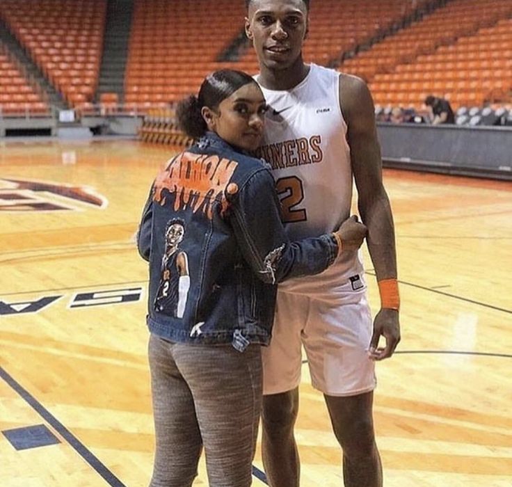 a man standing next to a woman on top of a basketball court in front of an arena