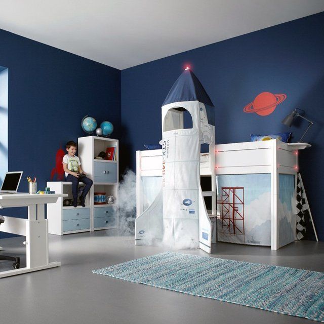 a child's bedroom with blue walls and white furniture, including a rocket ship bed