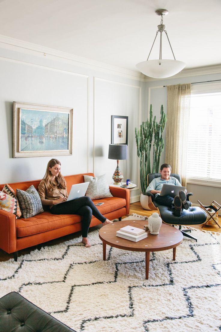 two people sitting on couches in a living room, one is using a laptop